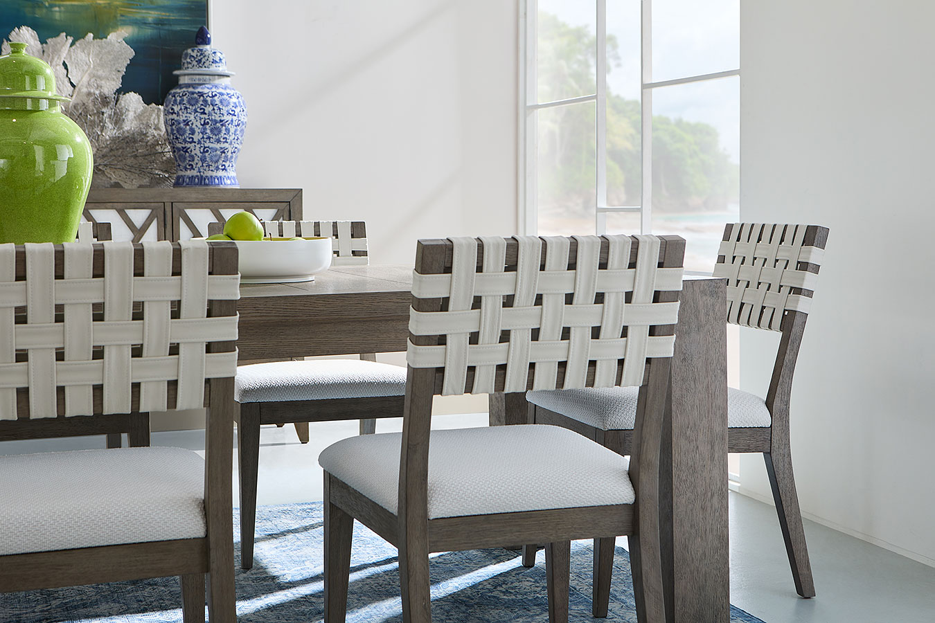 Dining room set with a wooden table and woven side chairs in a bright room.